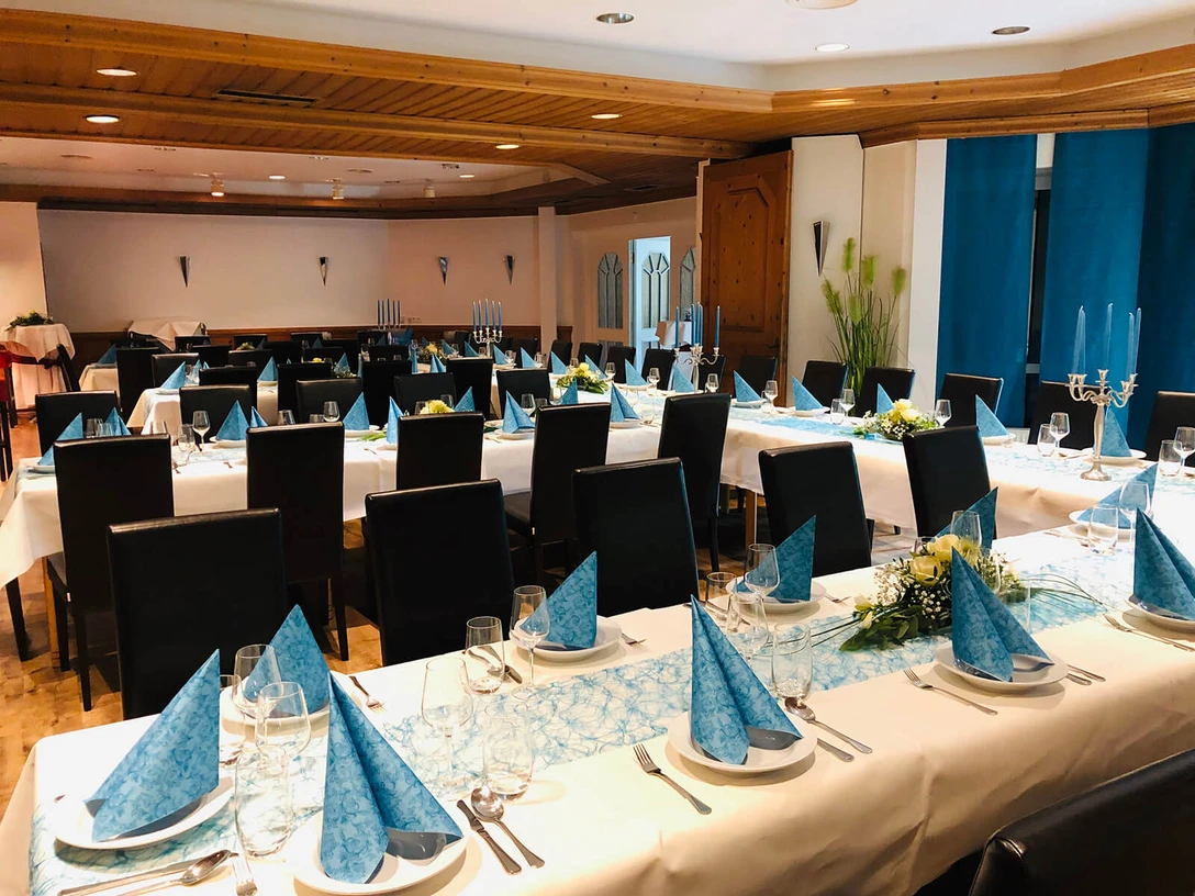 borchard.jpg Ein festlich eingedeckter Speisesaal mit schwarzen Stühlen, blauen Servietten und Kerzenständern.