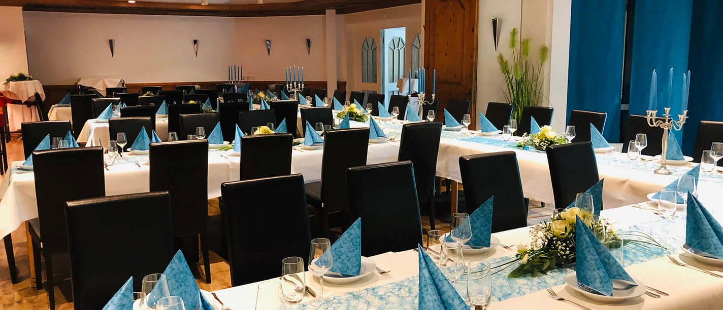 borchard.jpg Ein festlich eingedeckter Speisesaal mit schwarzen Stühlen, blauen Servietten und Kerzenständern.