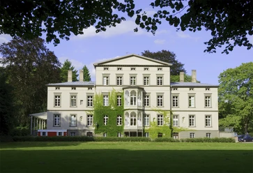 Villa Braunswerth Herrenhaus im klassizistischen Stil mit symmetrischer Fassade, umgeben von gepflegter Grünanlage.