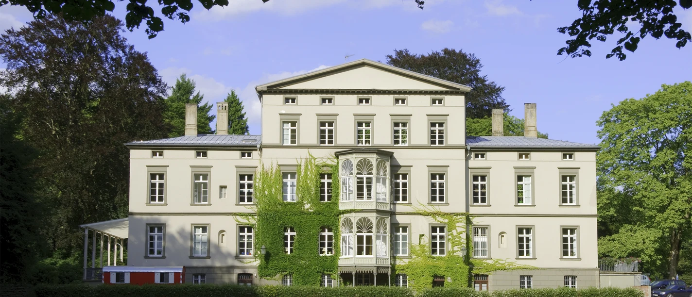 Villa Braunswerth Herrenhaus im klassizistischen Stil mit symmetrischer Fassade, umgeben von gepflegter Grünanlage.
