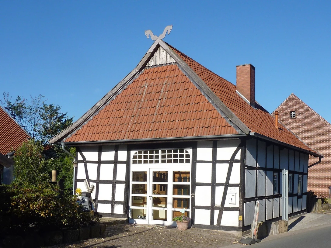Gästehaus Hartum Fachwerkhaus mit roten Dachziegeln, verziert mit Pferdeköpfen, umgeben von blauem Himmel und Bäumen.
