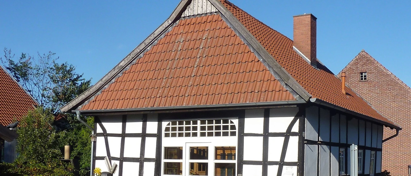 Gästehaus Hartum Fachwerkhaus mit roten Dachziegeln, verziert mit Pferdeköpfen, umgeben von blauem Himmel und Bäumen.