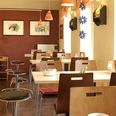 cafe vielfalt.jpg Ein helles Café mit modernen Holzmöbeln, orangefarbener Beleuchtung und Kunst an den Wänden.