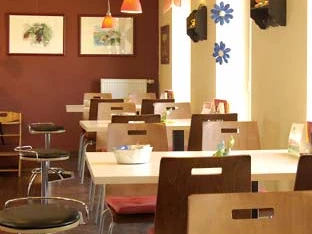 cafe vielfalt.jpg Ein helles Café mit modernen Holzmöbeln, orangefarbener Beleuchtung und Kunst an den Wänden.