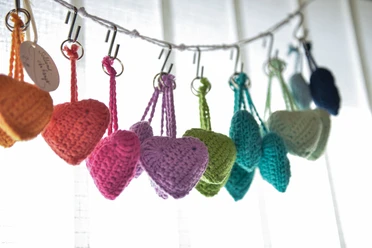 bunte Wollherzen Hobby Stübchen Handgehäkelte bunte Wollherzen hängen an Metallhaken an einer weißen Schnur.