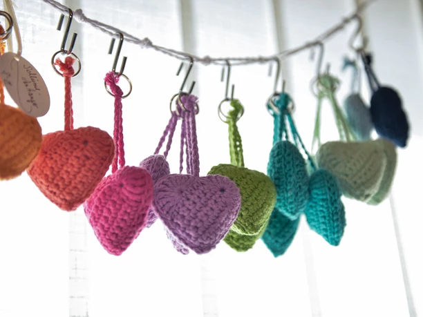 bunte Wollherzen Hobby Stübchen Handgehäkelte bunte Wollherzen hängen an Metallhaken an einer weißen Schnur.