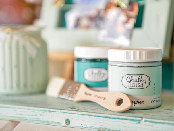 Hobby Stübchen Zwei Dosen Kreidefarbe in Mint und Petrol stehen mit einem Pinsel auf einer Holzablage.