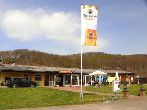 Ristorante Feuerland Ein breites Restaurant vor einem Wald. Davor weht eine Fahne mit Werbung für Benediktiner Bier.