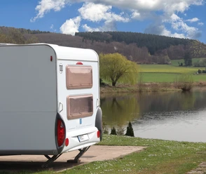 Camp Feuerland Ein Wohnwagen an einem See, im Hintergrund sieht man Wald auf einem Berg.