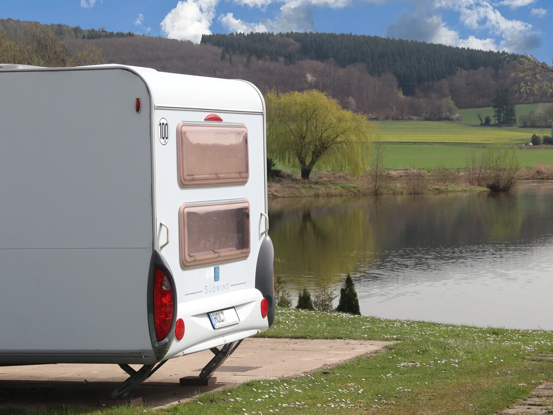Camp Feuerland Ein Wohnwagen an einem See, im Hintergrund sieht man Wald auf einem Berg.