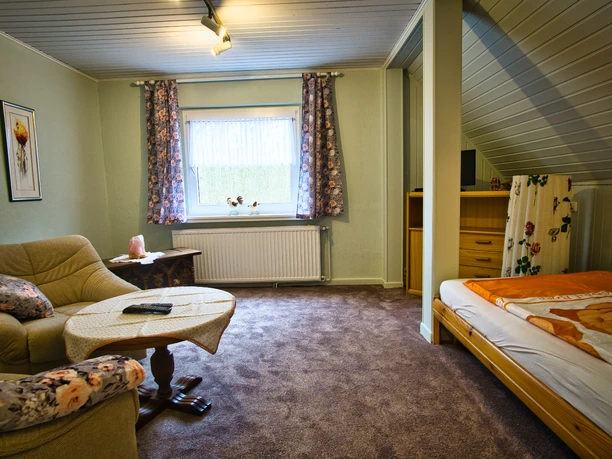Schlafzimmer 1 Wohn- und Schlafbereich mit Sesseln, Tisch am Fenster und einem Bett unter der Dachschräge.