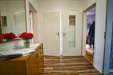 Wohnung-links-glüssing-11-amelinghausen (6).jpg Heller Flur mit Holzboden. Links eine Holzkommode mit Spiegel, roten Rosen und Gästebuch.