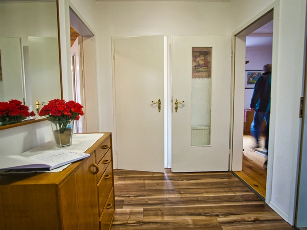 Wohnung Heller Flur mit Holzboden. Links eine Holzkommode mit Spiegel, roten Rosen und Gästebuch.