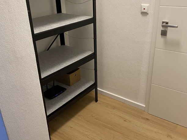 FeWo_Hille-Oberluebbe Schlichter Hausflur mit hellem Laminatboden, leerem Metallregal und weißer Tür in moderner Optik.