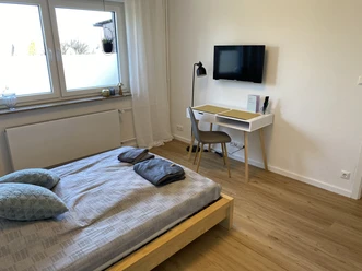 FeWo_Hille-Oberluebbe Ein helles Schlafzimmer mit Doppelbett, Bettwäsche, kleinem Schreibtisch, Stuhl und Flachbild-TV.