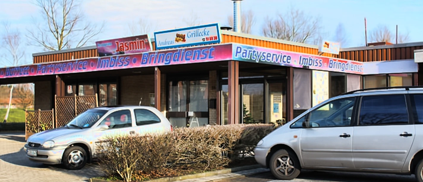 andreas-grill-ecke.jpg Zwei Autos parken vor einem Imbissgebäude namens "Andreas Grill Ecke" im Gewerbegebiet.