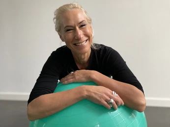 Konstanze Fernandez-Voß Konstanze Fernandez-Voß lächelt entspannt auf einem türkisfarbenen Gymnastikball im Innenraum.
