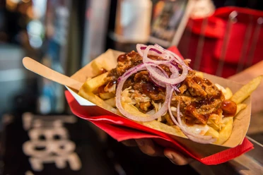 Cheatday Streetfood Festival Streetfood-Festival: Pommes im Pappbehälter, belegt mit Pulled Pork, Zwiebeln und BBQ-Sauce.