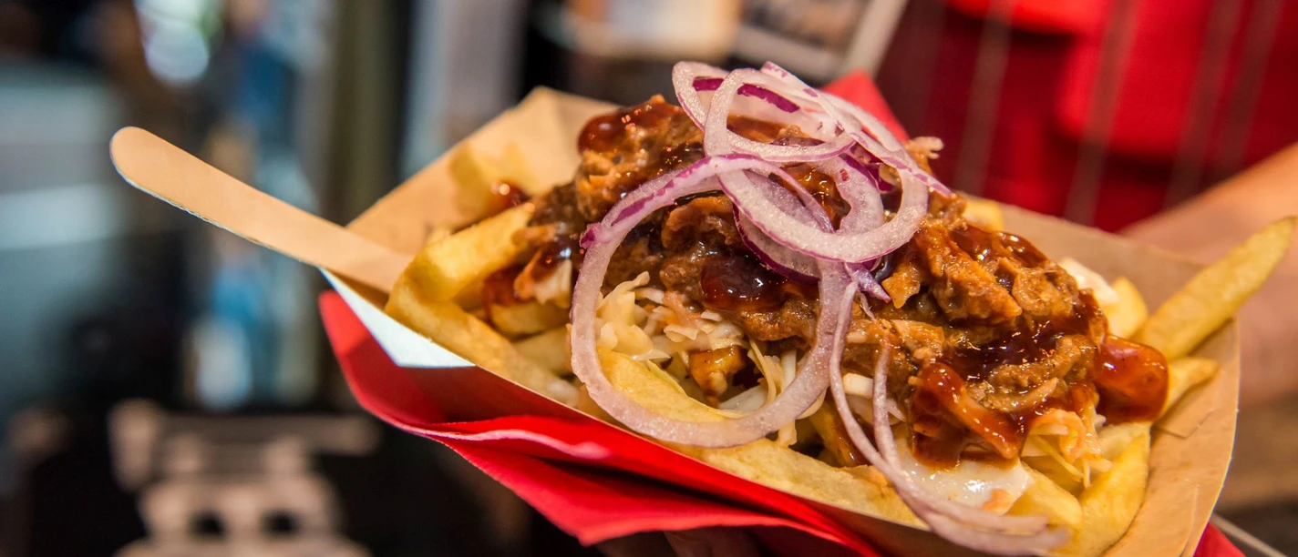 Cheatday Streetfood Festival Streetfood-Festival: Pommes im Pappbehälter, belegt mit Pulled Pork, Zwiebeln und BBQ-Sauce.