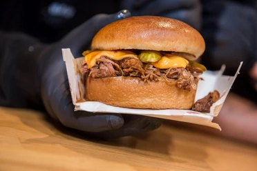 Cheatday Streetfood Festival Ein saftiger Burger mit geschmolzenem Käse und eingelegten Gurken wird nah gezeigt.