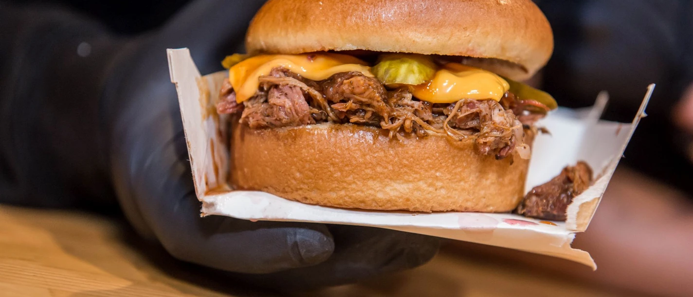 Cheatday Streetfood Festival Ein saftiger Burger mit geschmolzenem Käse und eingelegten Gurken wird nah gezeigt.