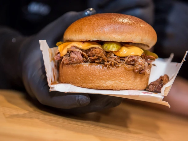 Cheatday Streetfood Festival Ein saftiger Burger mit geschmolzenem Käse und eingelegten Gurken wird nah gezeigt.