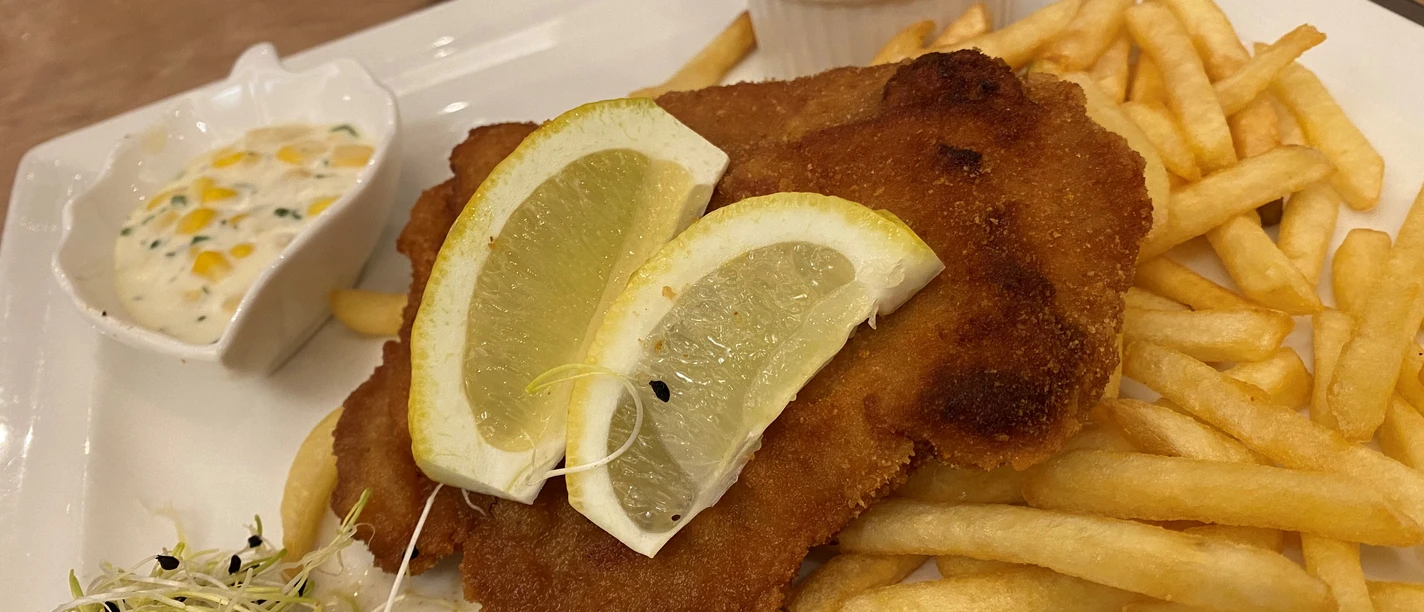 Two lemon slices on a crispy schnitzel, served with chips and herb dip, decorated with sprouts.
