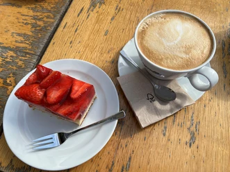 Coffee cup with latte art and piece of strawberry cake on wooden table, ready to enjoy.