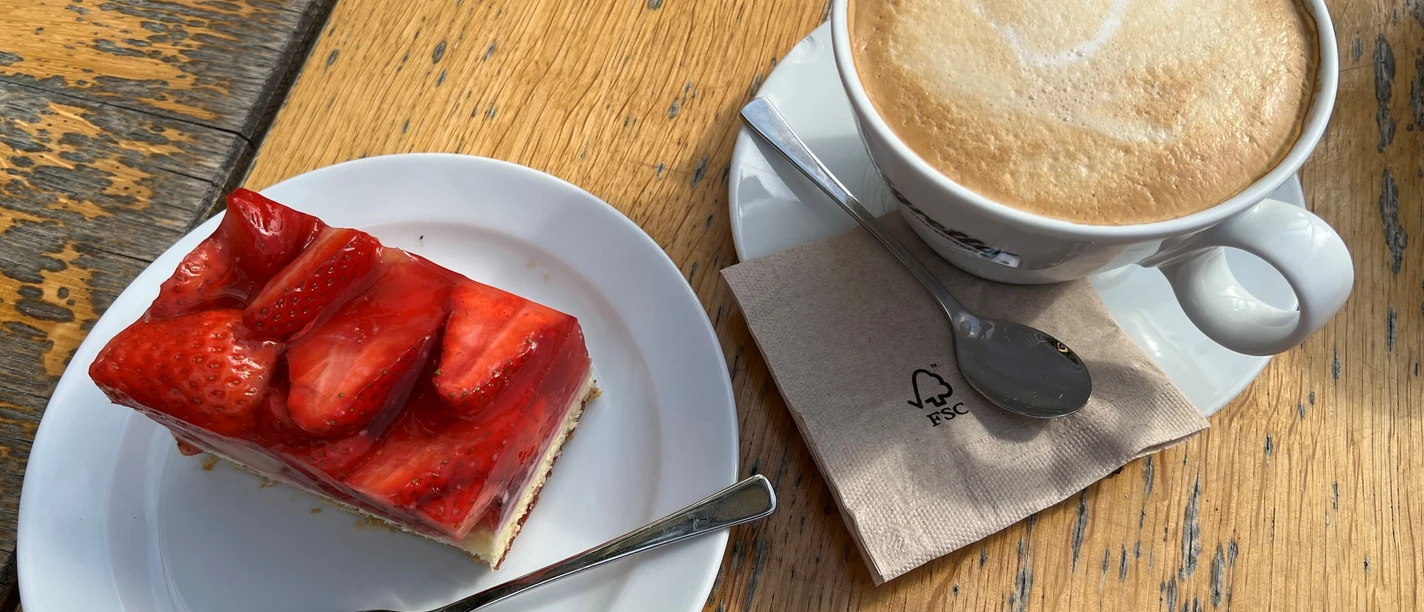 Kaffee und Kuchen Kaffeetasse mit Latte Art und Erdbeerkuchenstück auf Holztisch, bereit zum Genuss.