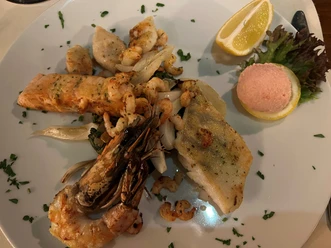 Griechischer Teller Eine vielfältige Auswahl von Meeresfrüchten und Fischfilets mit Zitrone und Garnitur auf einem Teller.