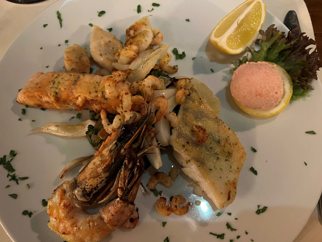 Griechischer Teller Eine vielfältige Auswahl von Meeresfrüchten und Fischfilets mit Zitrone und Garnitur auf einem Teller.