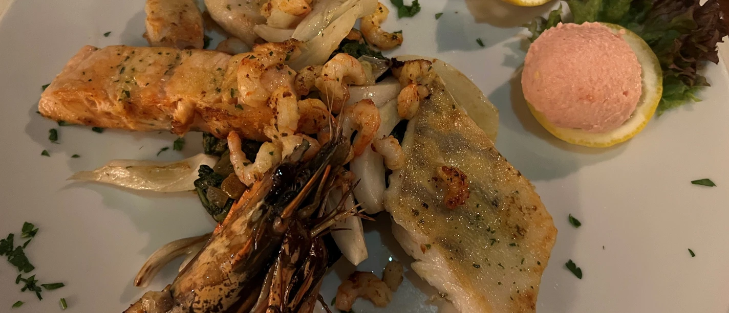 Griechischer Teller Eine vielfältige Auswahl von Meeresfrüchten und Fischfilets mit Zitrone und Garnitur auf einem Teller.