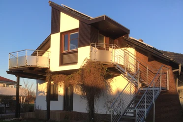 Ferienwohnung Ruhepol Zweistöckige Ferienwohnung mit moderner Fassade, Balkon und Außentreppe unter blauem Himmel.
