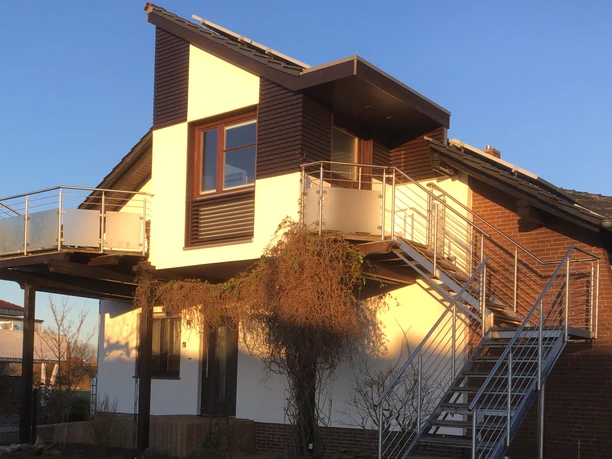 Ferienwohnung Ruhepol Zweistöckige Ferienwohnung mit moderner Fassade, Balkon und Außentreppe unter blauem Himmel.