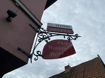 Das Bild zeigt ein traditionelles Wirtshaus-Schild mit der Aufschrift "Dat Wählige Rott" und "Hotel".