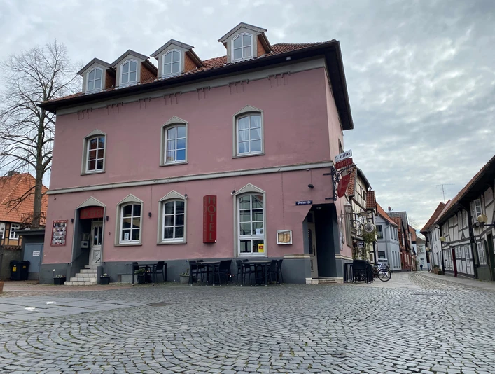 Historisches rosafarbenes Gebäude mit Hotel, an einer gepflasterten Straße gelegen, mehrere Fenster und Dachgauben.