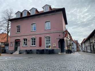 Pup Dat Wählige Rott Historisches rosafarbenes Gebäude mit Hotel, an einer gepflasterten Straße gelegen, mehrere Fenster und Dachgauben.