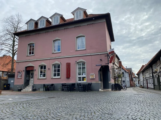 Pup Dat Wählige Rott Historisches rosafarbenes Gebäude mit Hotel, an einer gepflasterten Straße gelegen, mehrere Fenster und Dachgauben.