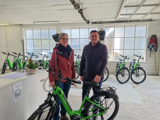 e-bike-verleih-bad-zwischenahn-räder.jpg Zwei Personen stehen in einem Raum voller grüner E-Bikes; sie wirken freundlich.