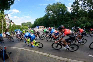 Rennen "Rund in Refrath" Rennradfahrer in einem Wettbewerb rasen eine kurvige Straße entlang, umgeben von Bäumen.