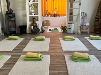 Yoga-Raum Heller Yoga-Raum mit sechs Matten, gelben Decken, Buddha-Statue und einladendem Ambiente.