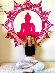 Heidi Lödige Yoga Eine Frau in weißer Hose und schwarzem Shirt meditiert vor einer pinken Buddha-Silhouette an der Wand.