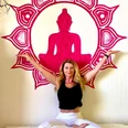 Heidi Lödige Yoga Eine Frau in weißer Hose und schwarzem Shirt meditiert vor einer pinken Buddha-Silhouette an der Wand.