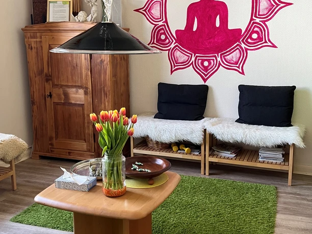 Eingangsbereich Ein einladender Raum mit Holzdekor, rosa Buddha-Wandbild, gemütlichen Sitzbänken und Frühlingsblumen.