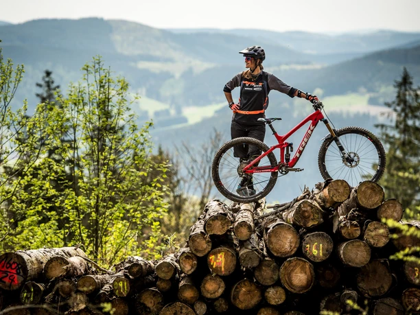 Bikerin mit Mountainbike auf Holzstapel Bikerin mit Mountainbike auf Holzstapel