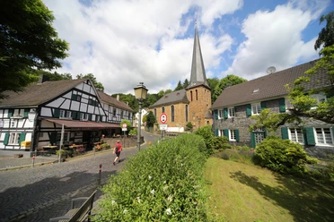 Volberg mit Kirche Malerisches Dorf mit Fachwerkhäusern, einer Kirche mit hohem Turm und gepflasterten Straßen bei Sonnenschein.