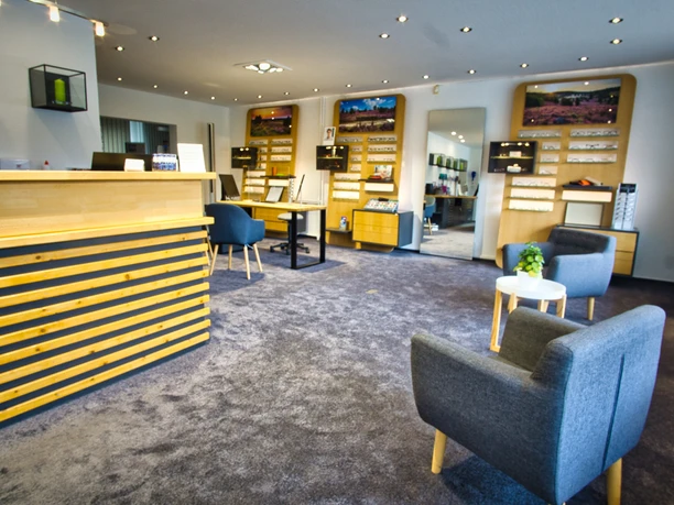 Brillen Ein heller Verkaufsraum eines Optikers mit Holztheke, Brillenregalen und grauen Sesseln.