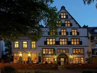 Galerie-Hotel Abdinghof Fachwerkhaus mit leuchtenden Fenstern am Abend, umgeben von Bäumen und Holzzaun, lädt zum Verweilen ein.