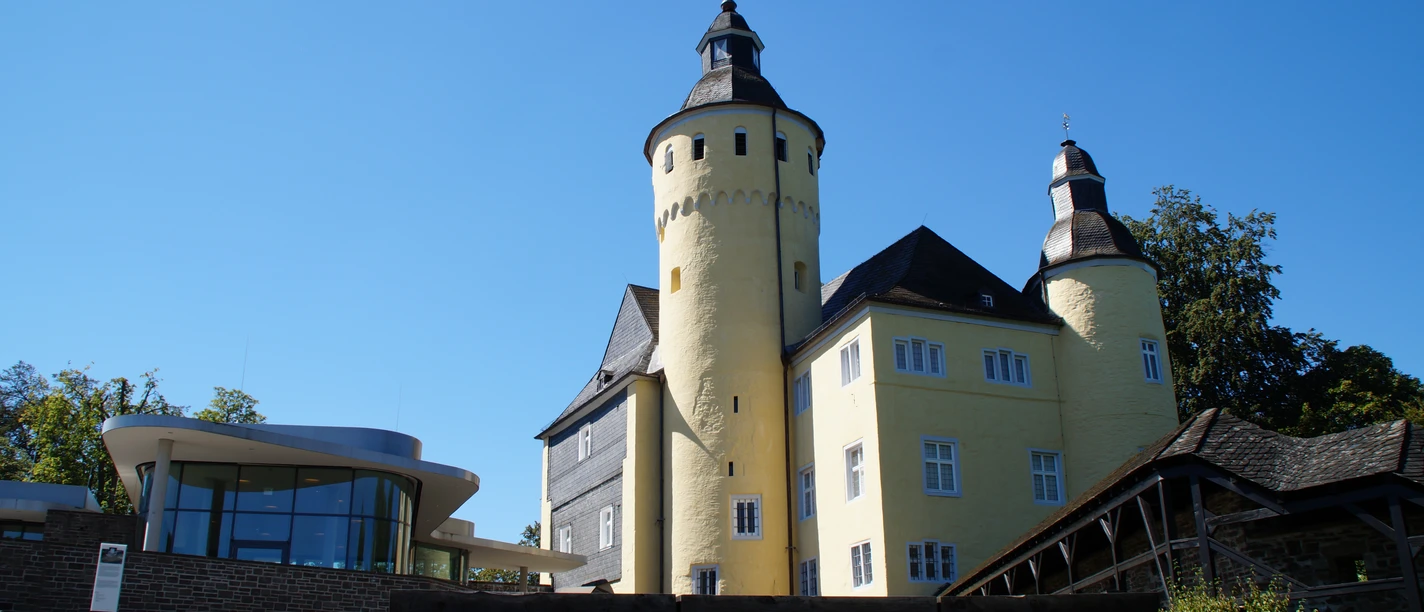 Historisches Schloss mit gelber Fassade und Türmen, flankiert von moderner Glasarchitektur.