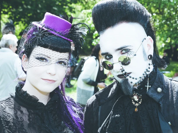 danny.sotzny02.jpg Ein Paar in schwarzer, viktorianischer Goth-Kleidung und pastellfarbenen Accessoires im Freien.